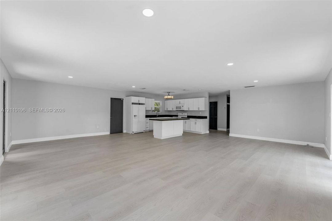 Open-concept interior featuring light wood-finish flooring, recessed lighting, and a kitchen equipped with white cabinetry, a center island, and dark-toned countertops