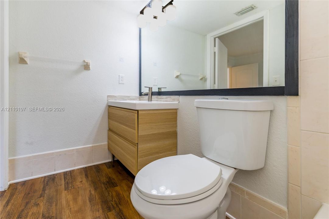 Wood-finish floating vanity with a white rectangular sink, framed wall-to-wall mirror, multi-globe vanity light fixture, and wood-finish flooring