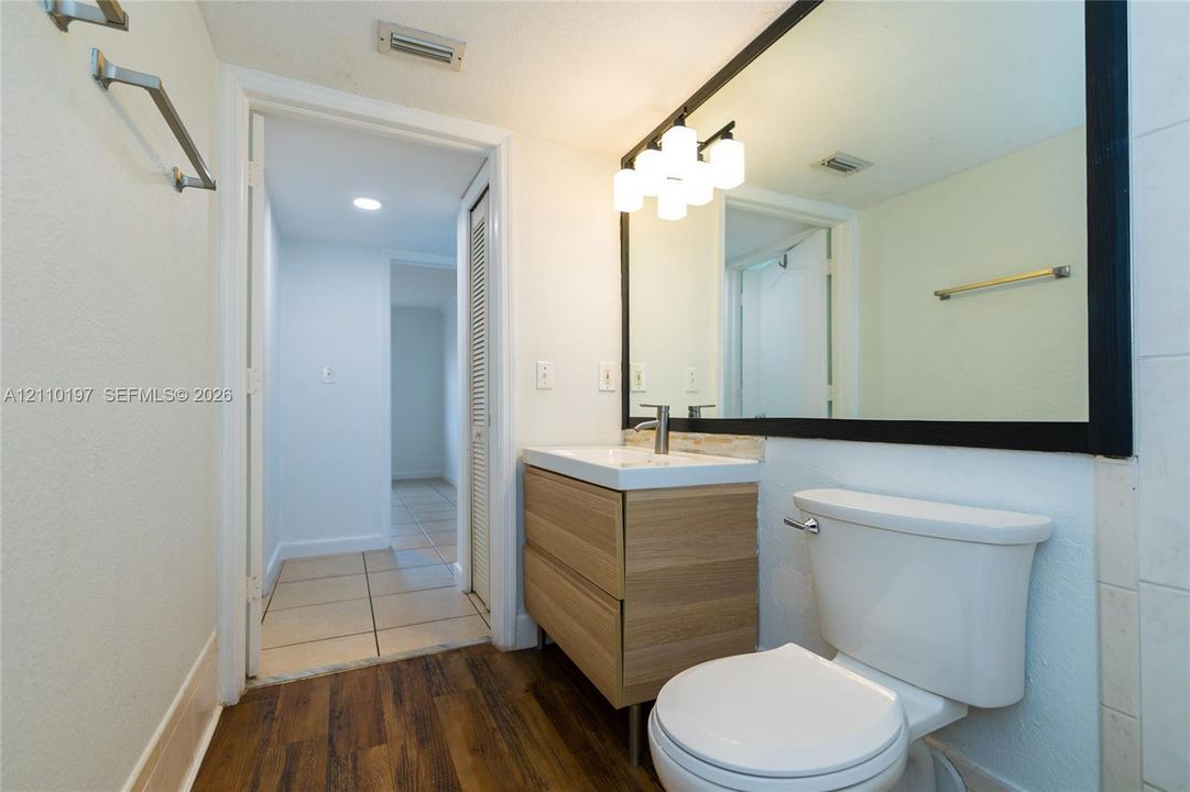 Bathroom featuring a wood-finish vanity with a clean-lined basin, a large mirror with a bold black frame, multi-bulb wall lighting, and wood-finish flooring
