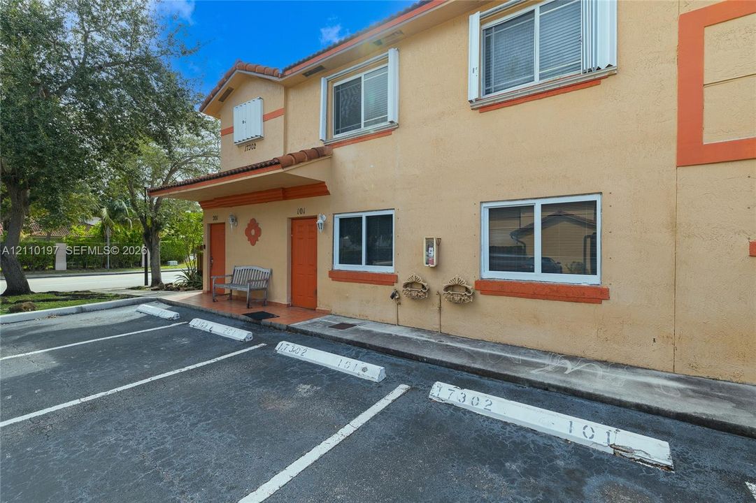 Stucco exterior facade featuring a clay-tiled roofline, orange trim accents, and dedicated surface parking