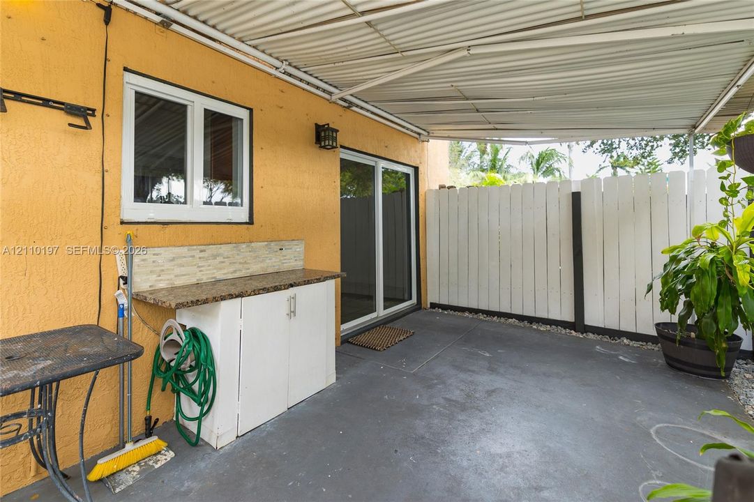 Covered concrete patio featuring built-in cabinetry with stone-finish countertop, tiled backsplash, and privacy fencing