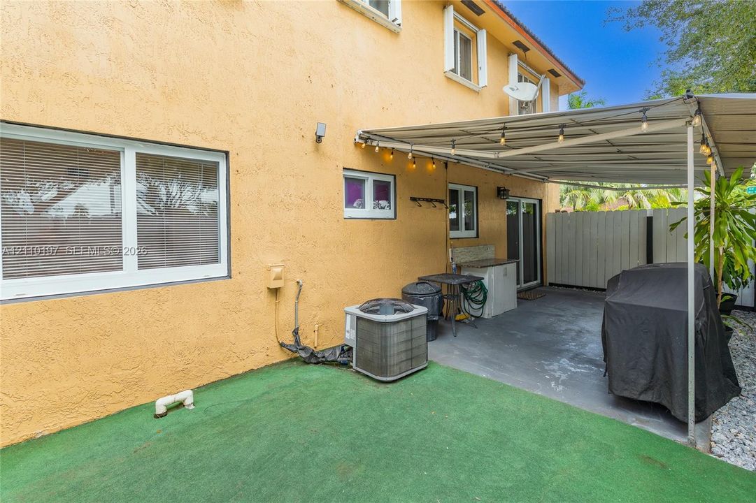 Stucco exterior featuring a covered patio, concrete flooring, exterior string lighting, and white-framed windows