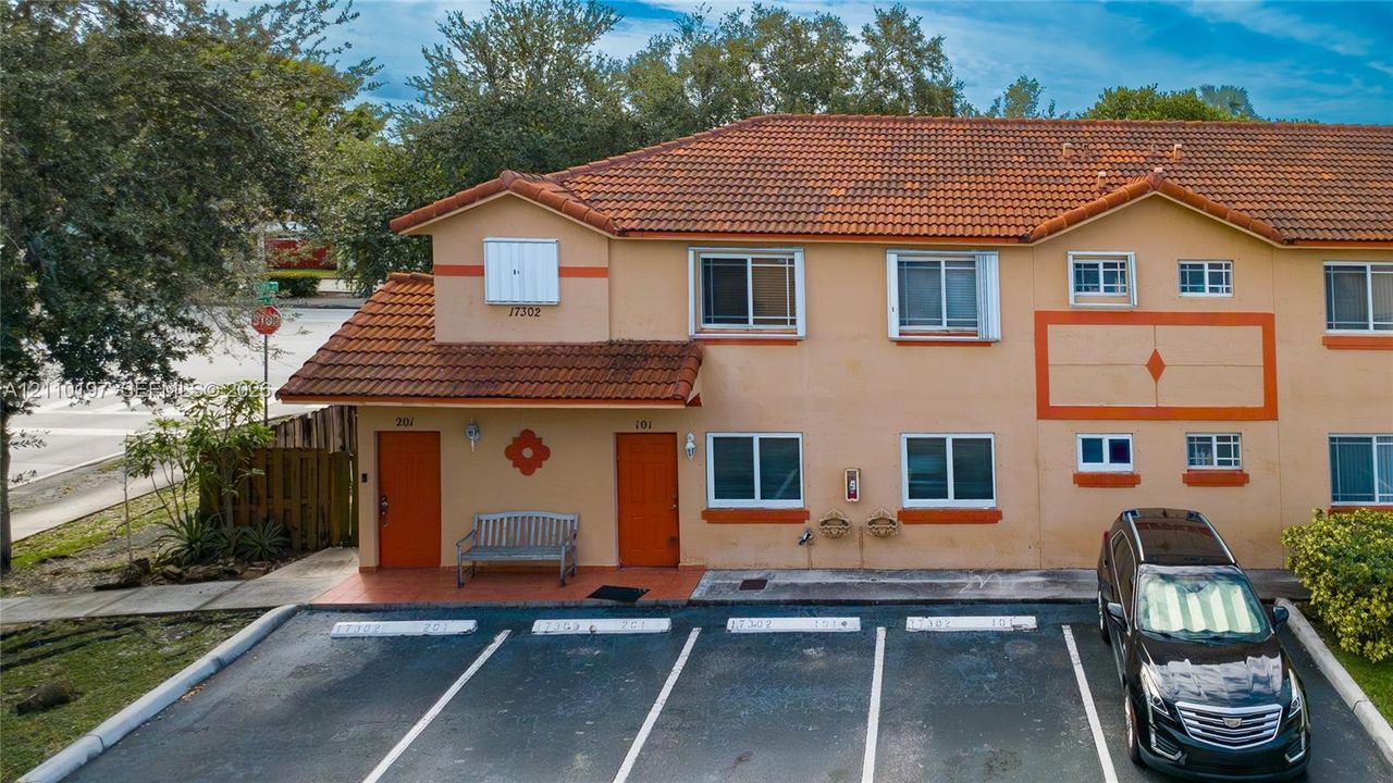 Two-story exterior featuring a clay tile roof, stucco facade, and dedicated paved parking spaces