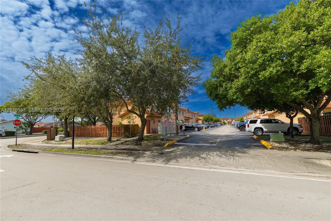 Exterior view featuring multi-unit structures with stucco siding, paved surface parking, and mature trees
