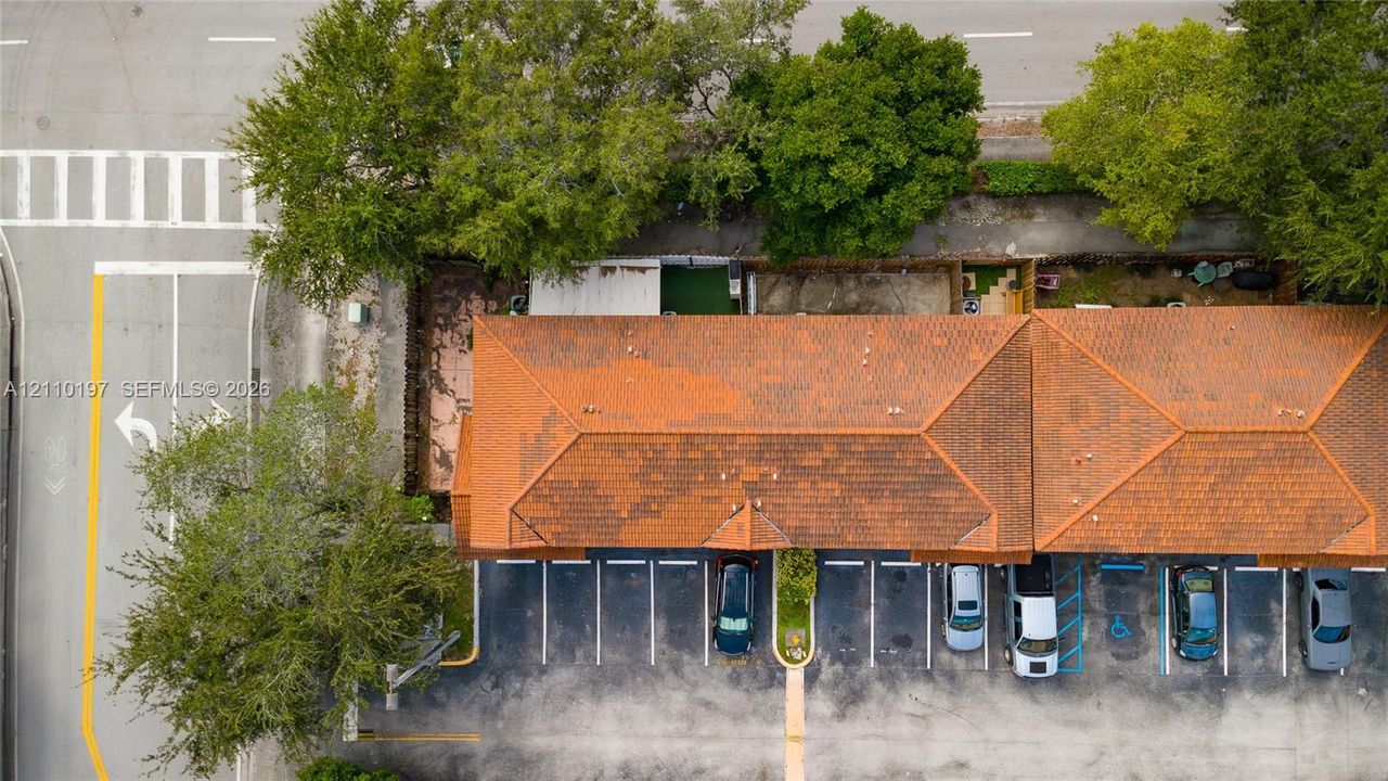 Aerial perspective of a multi-unit property featuring a terra cotta tile roof and a paved surface parking lot