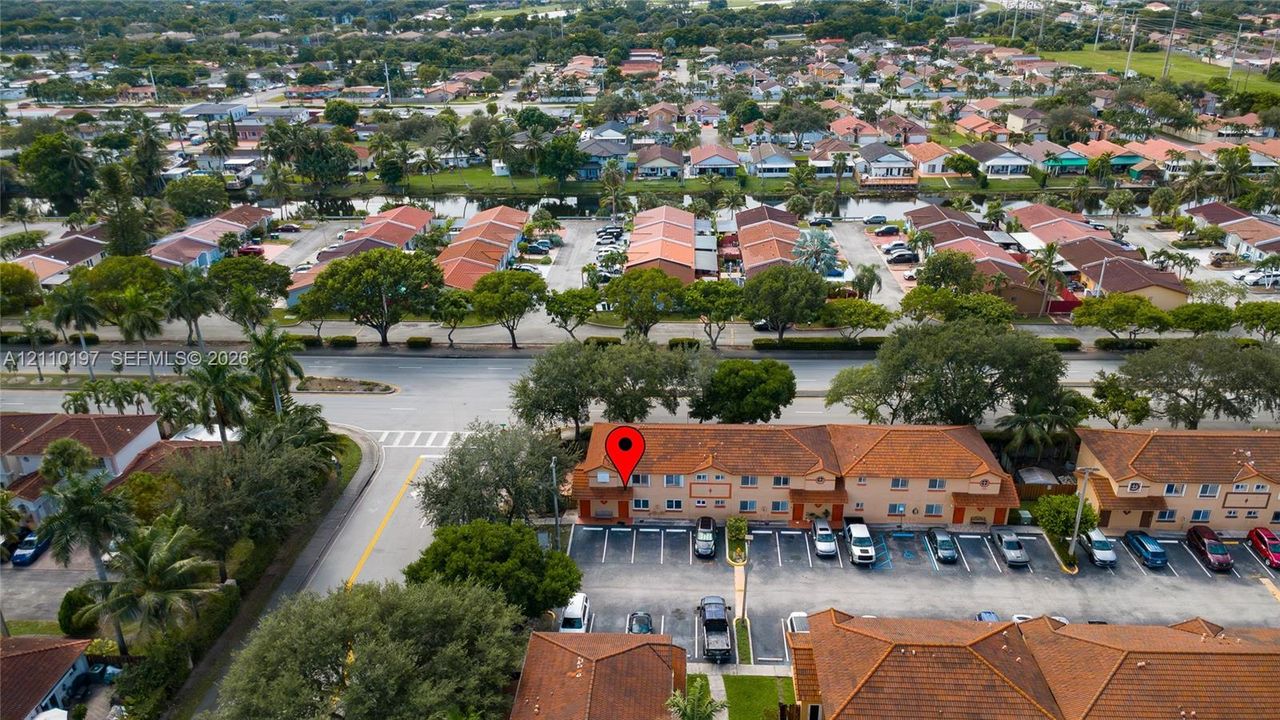 Aerial perspective of a multi-story residential building featuring a tile roof, tan stucco facade, and an integrated asphalt parking lot