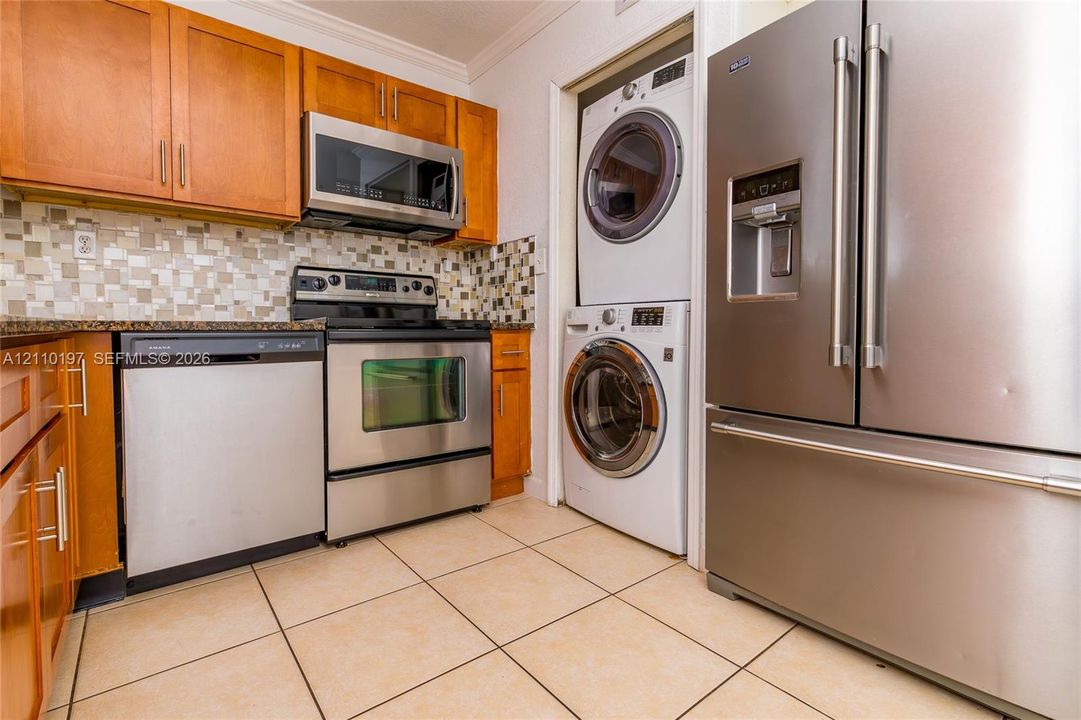 Kitchen featuring wooden cabinetry, mosaic tile backsplash, stainless steel appliances, and a stacked washer and dryer unit