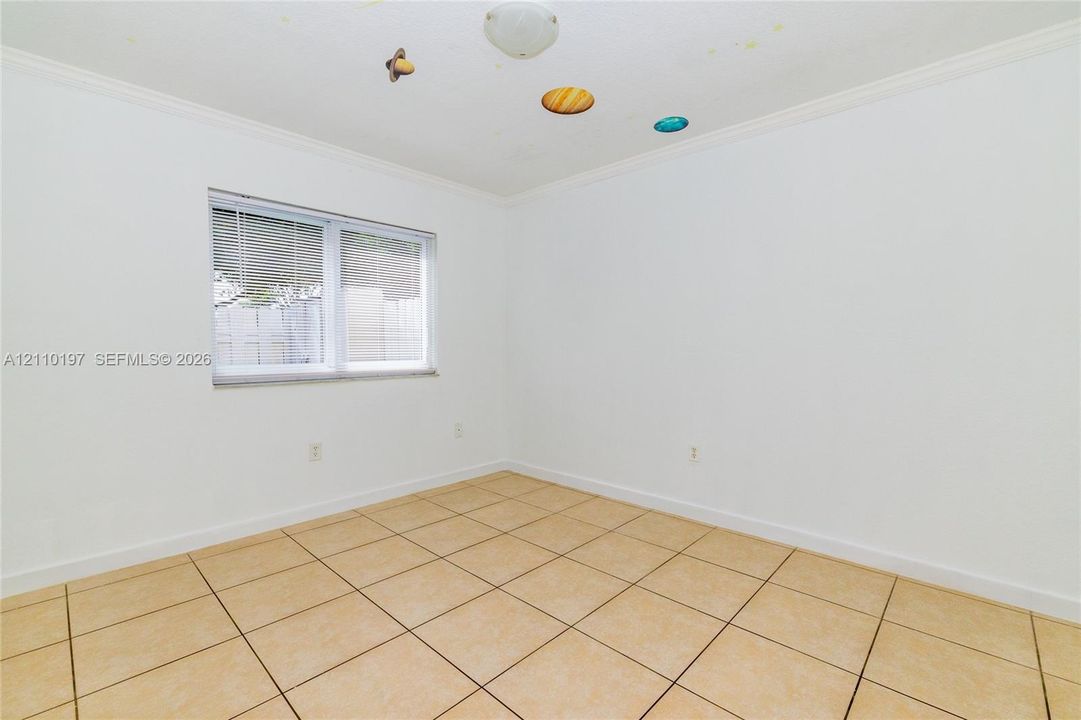 Interior space featuring neutral wall tones, large-format tile flooring, crown molding, and a dual-pane window with integrated blinds