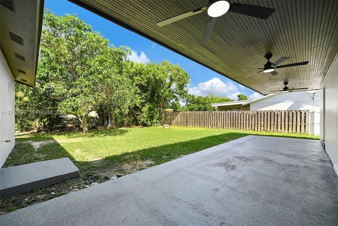 Covered patio featuring recessed ceiling fans, concrete flooring, and a fenced backyard with mature trees