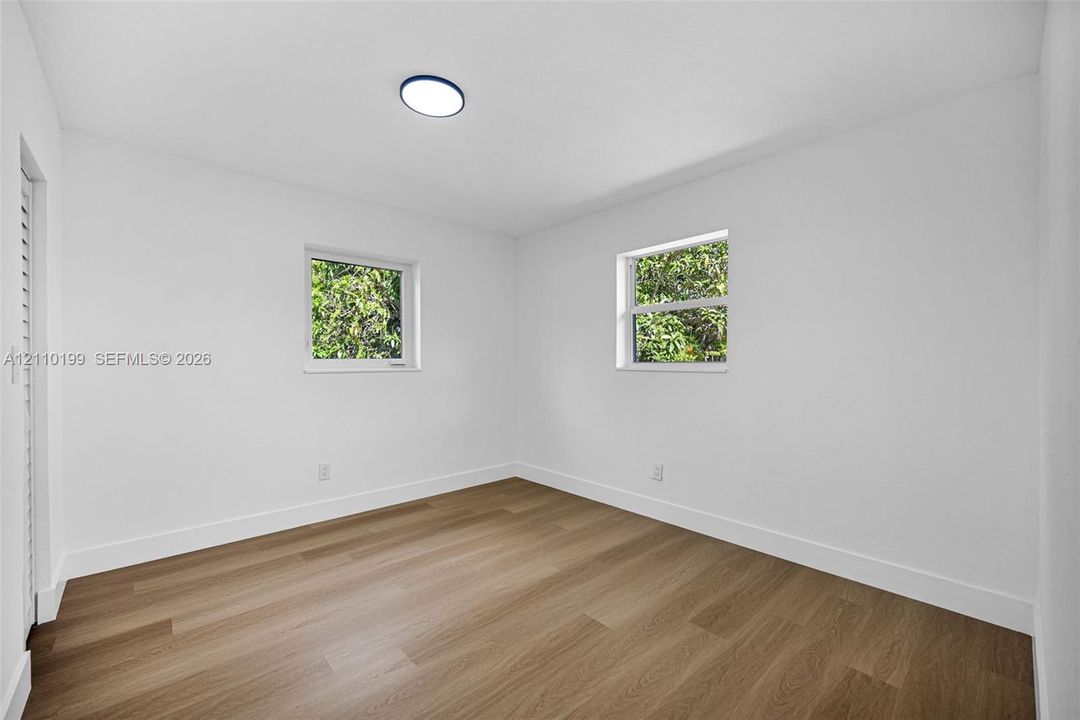 Room featuring wood-finish flooring, white walls, dual windows, and a flush-mount ceiling light