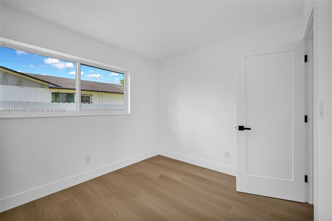 Room featuring wood-finish flooring, a horizontal sliding window, and a white interior door with matte black hardware