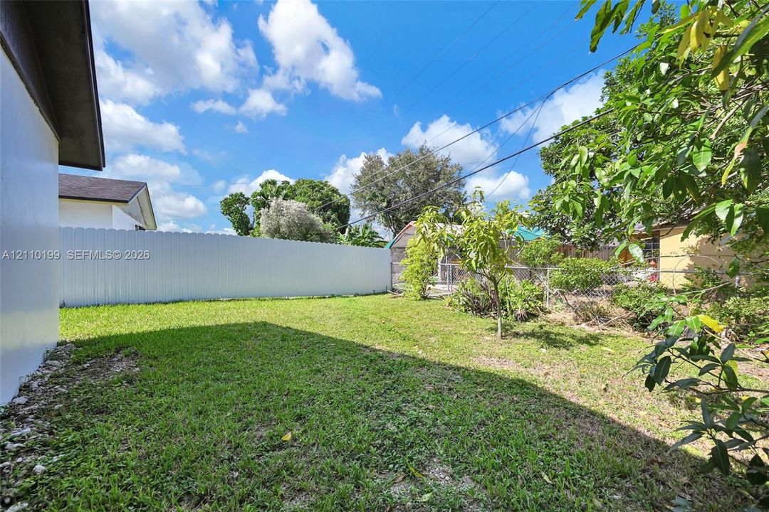 Rear yard featuring a grass lawn, solid vinyl fencing, and mature trees