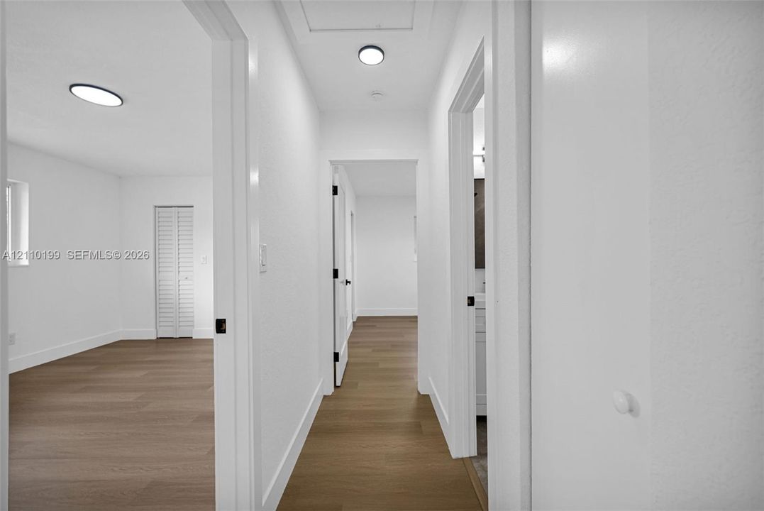 Hallway featuring wood-finish flooring, white walls, flush-mount circular lighting, and louvered closet doors