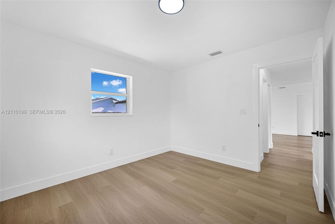 Neutral interior room featuring white-painted walls, wood-finish flooring, a single-hung window, and a recessed ceiling light fixture