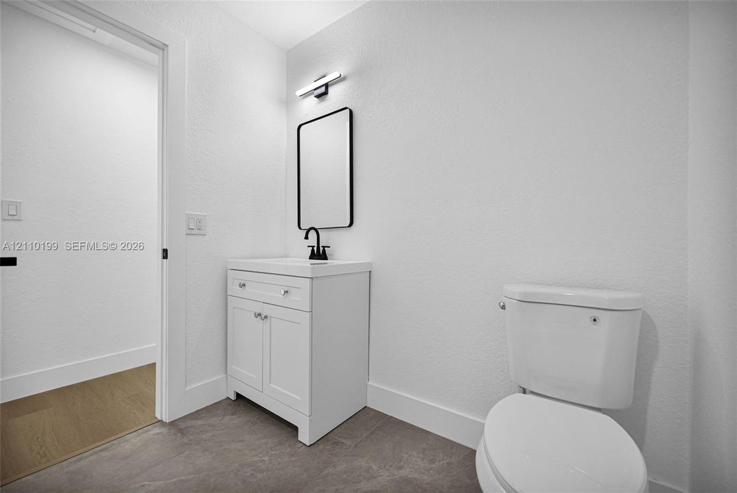 White vanity with storage cabinet, rectangular sink, matte black faucet, rectangular mirror, and matte black wall-mounted vanity light fixture