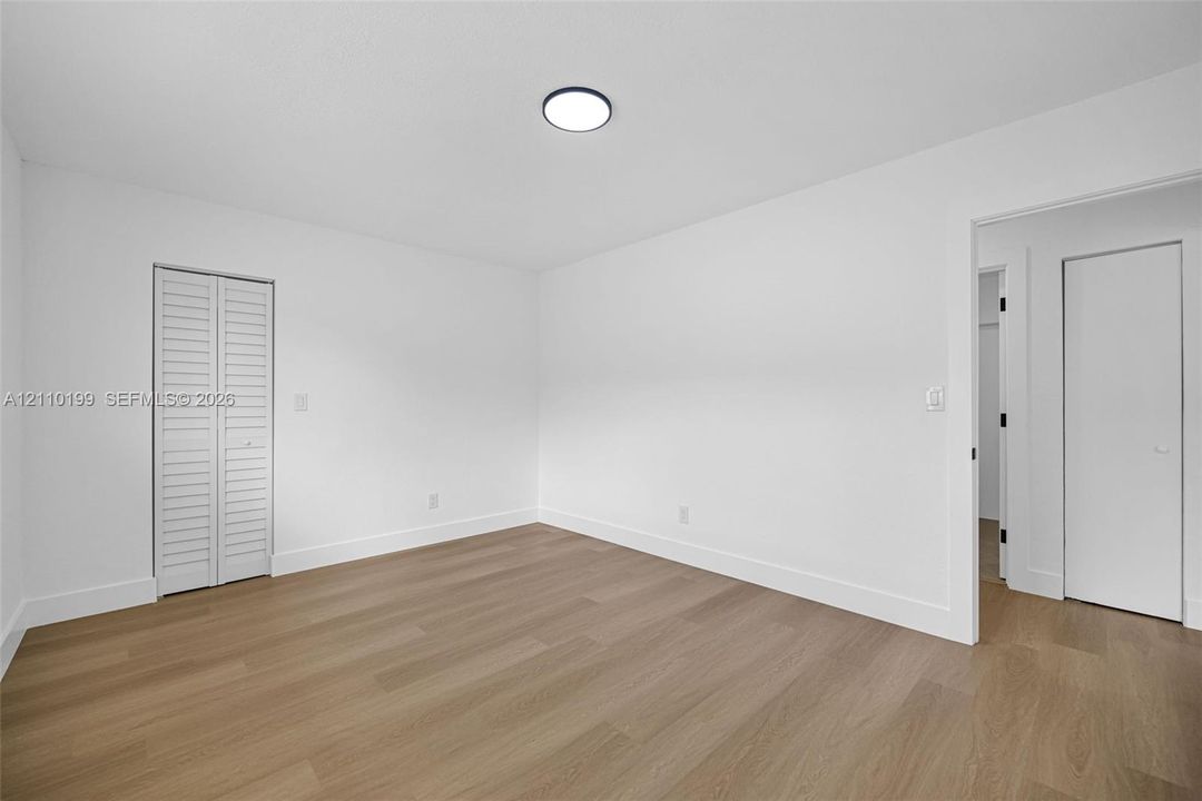 Neutral wall finishes, wood-finish flooring, white louvered bifold closet doors, and flush-mount ceiling lighting