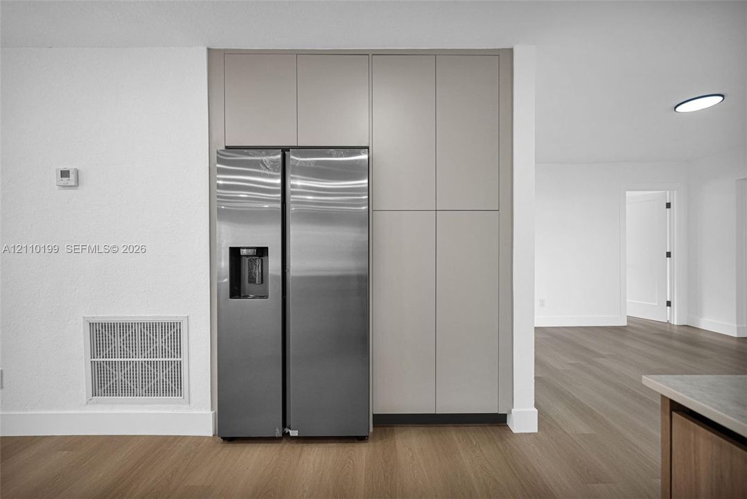 Floor-to-ceiling cabinetry with a matte neutral finish, integrated stainless steel side-by-side refrigerator, and wood-finish flooring