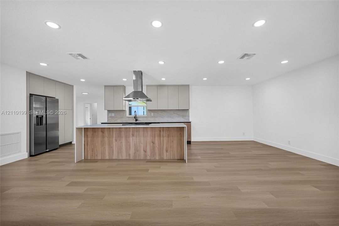 Kitchen featuring flat-panel cabinetry, a central island with wood-finish paneling, a stainless steel chimney-style range hood, and wood-finish flooring throughout