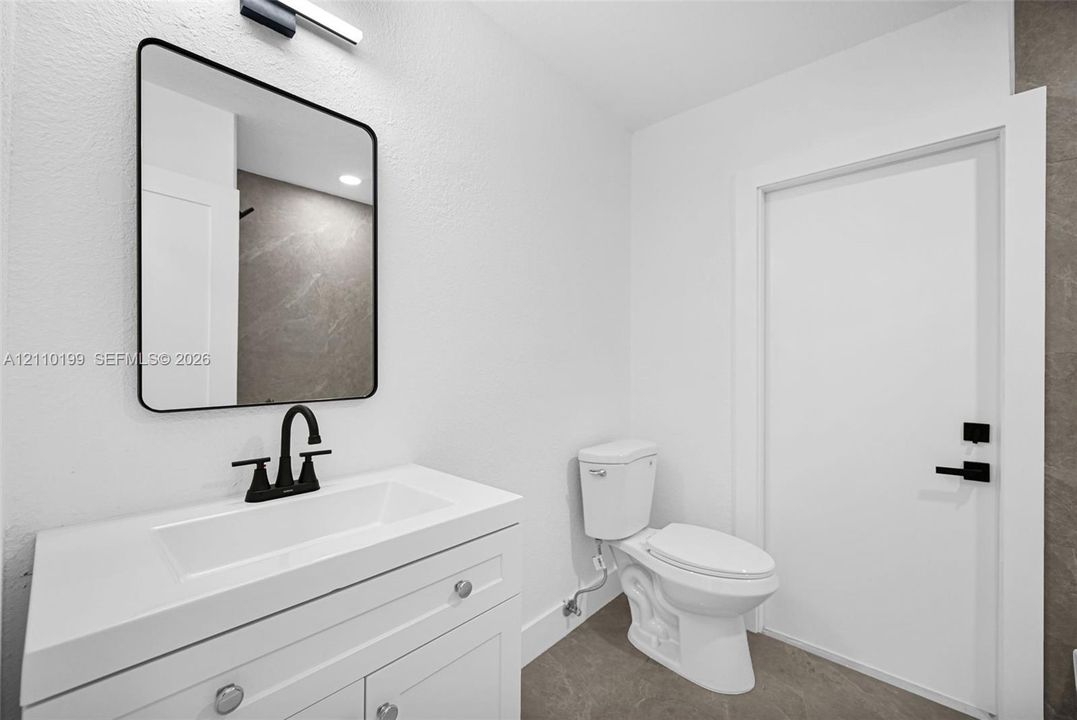 White vanity featuring an integrated rectangular sink and stone-surface countertop, matte black faucet, rectangular mirror with a black frame, and matte black door hardware