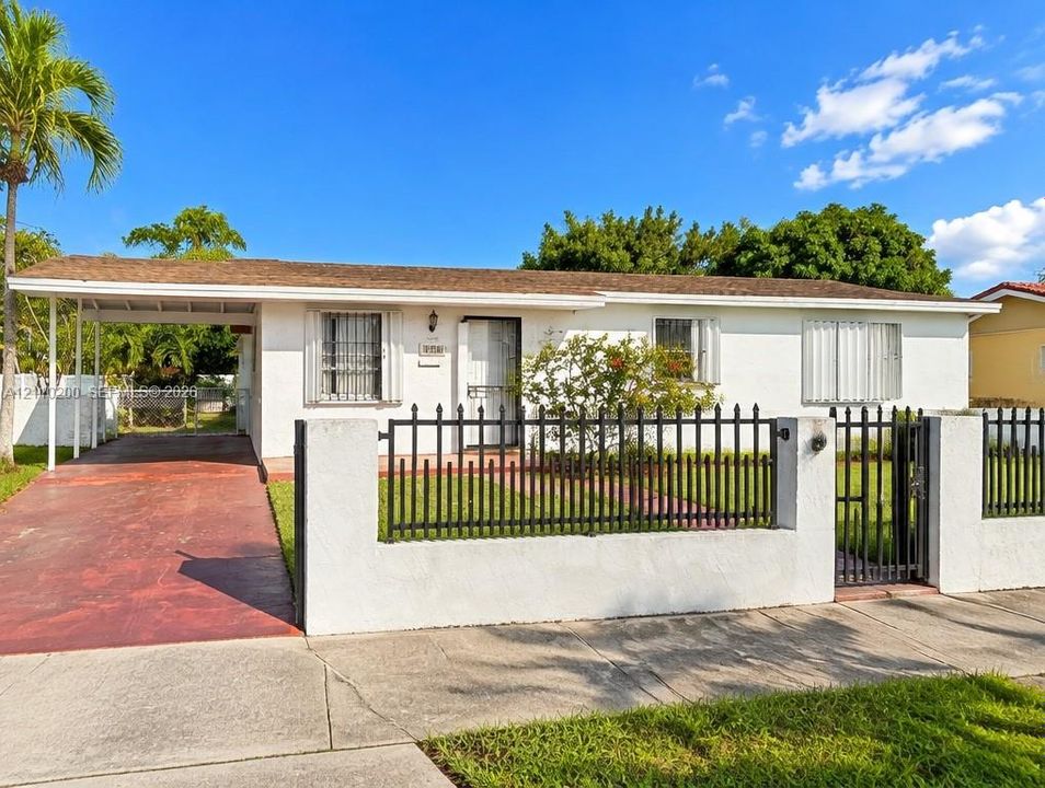 Single-story residence featuring a painted masonry exterior, covered carport, and perimeter metal fencing with concrete pillars