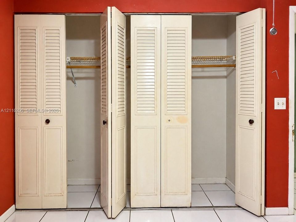 Double bi-fold louvered closet doors with integrated hanging rods, wire shelving, and neutral tile flooring