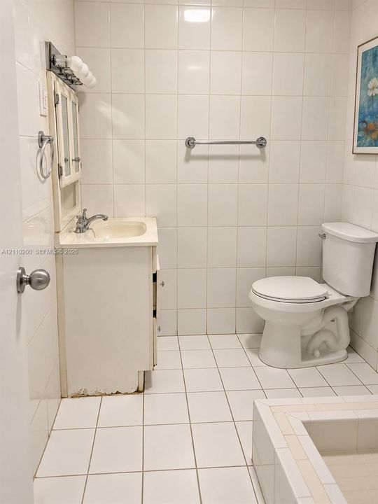 Full-height wall tiling, white vanity cabinet with a integrated sink, chrome faucet fixture, matching white ceramic floor tiling, and a built-in tub with tile surround