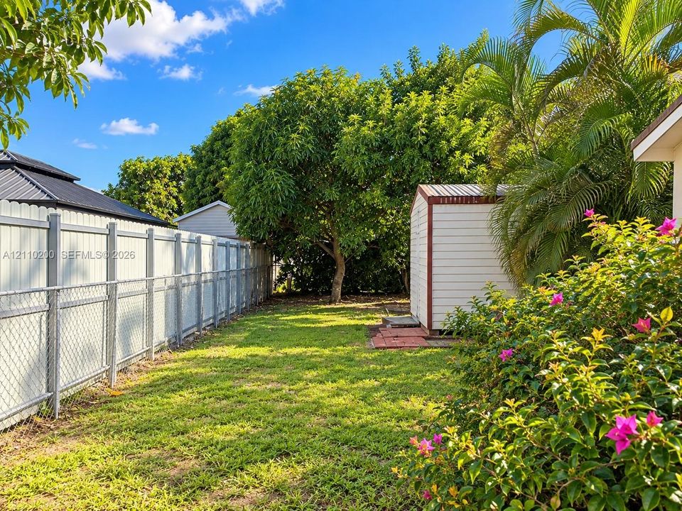 Backyard featuring a grass lawn, metal fencing, a detached storage shed, mature trees, and landscaping