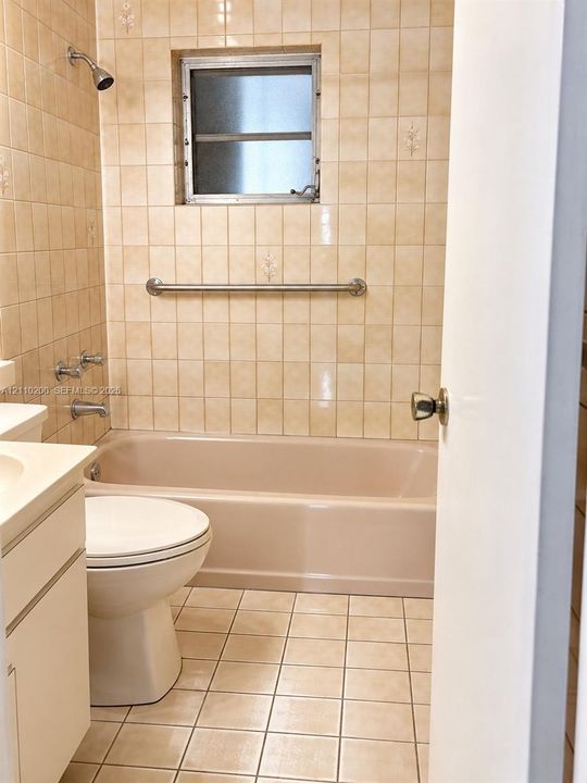 Bathroom featuring a full-sized bathtub, floor-to-ceiling tile surrounds, a built-in metal grab bar, ceramic tile flooring, and a window for natural light