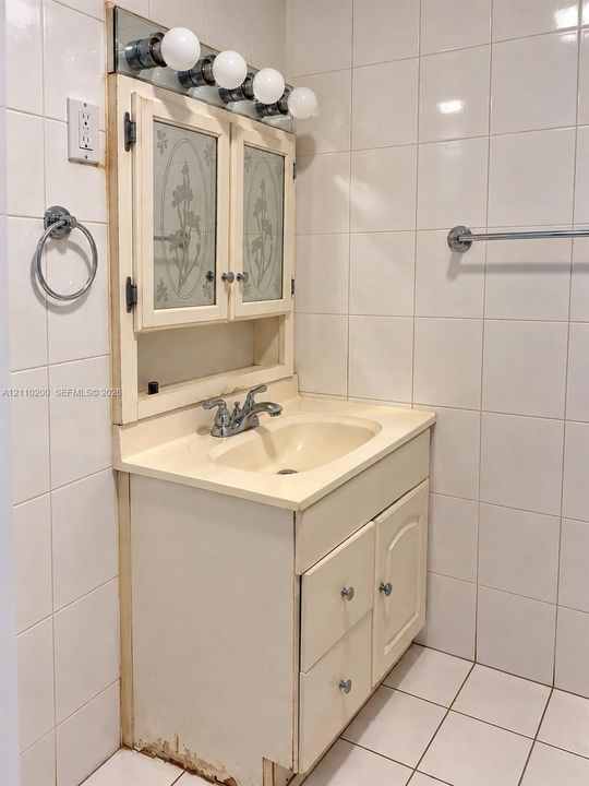 Bathroom vanity featuring a molded sink basin, integrated cabinetry with etched glass-panel storage, chrome-finish fixtures, and a five-light vanity bar