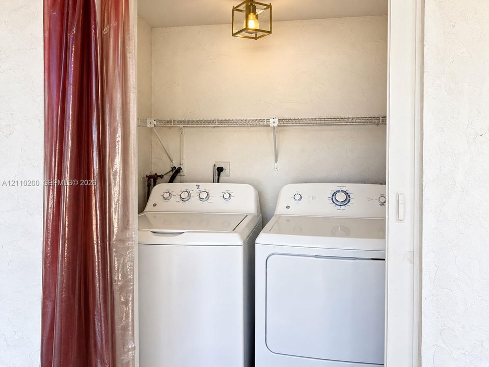 Laundry alcove featuring a wall-mounted wire storage shelf and a geometric brass-finish flush mount light fixture