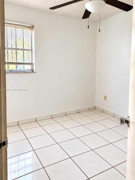 Room featuring large-format white tile flooring, neutral walls, and a ceiling-mounted light fixture with a fan