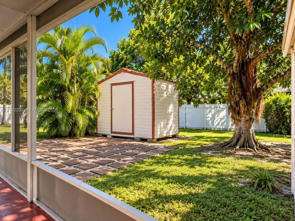 Backyard featuring a paved patio area, detached storage shed, mature trees, and perimeter vinyl fencing