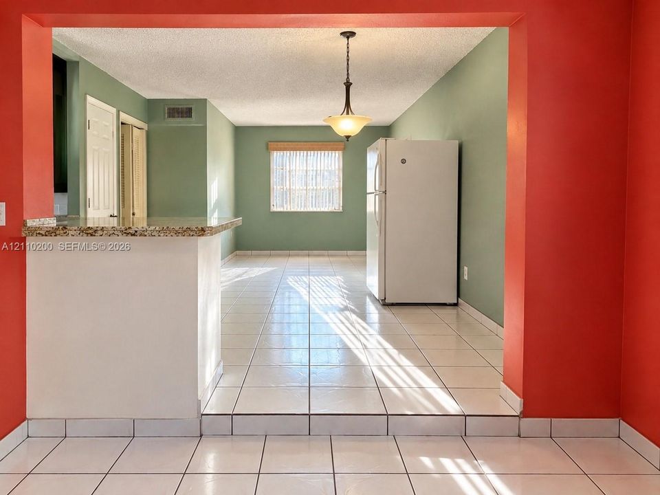 Open-concept interior featuring tiled flooring, a stone-surfaced breakfast bar, and a single-pendant light fixture