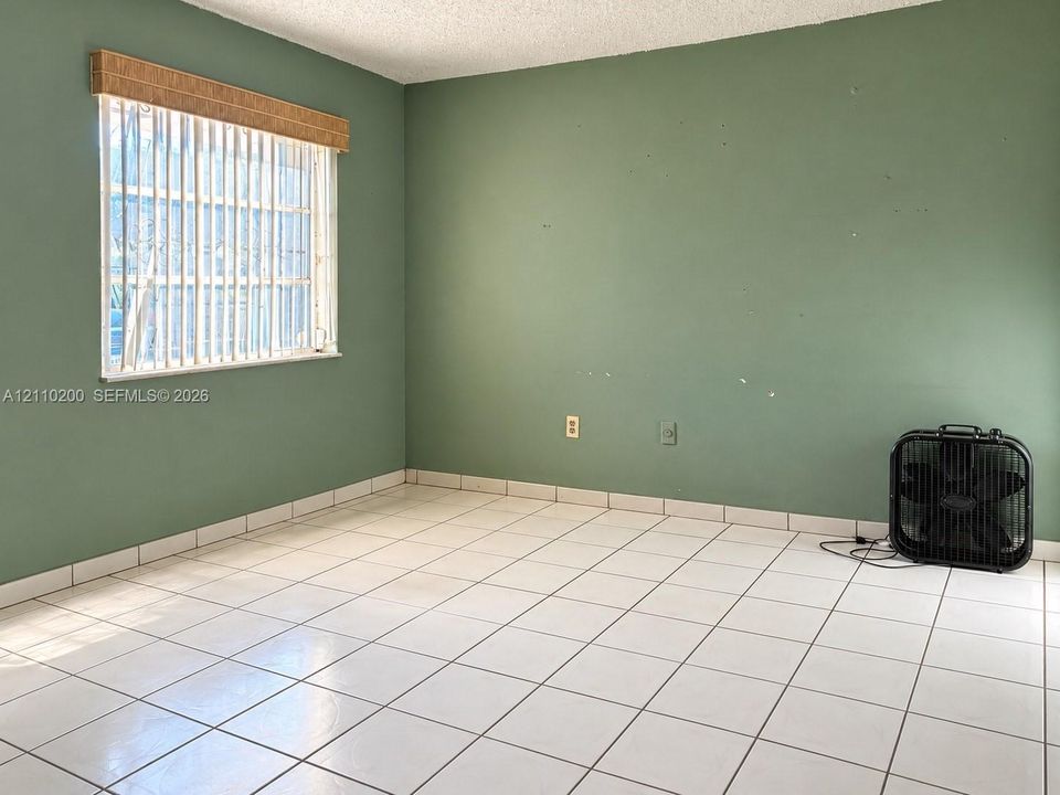 Room featuring neutral tile flooring, light green walls, and a window with a woven roman shade