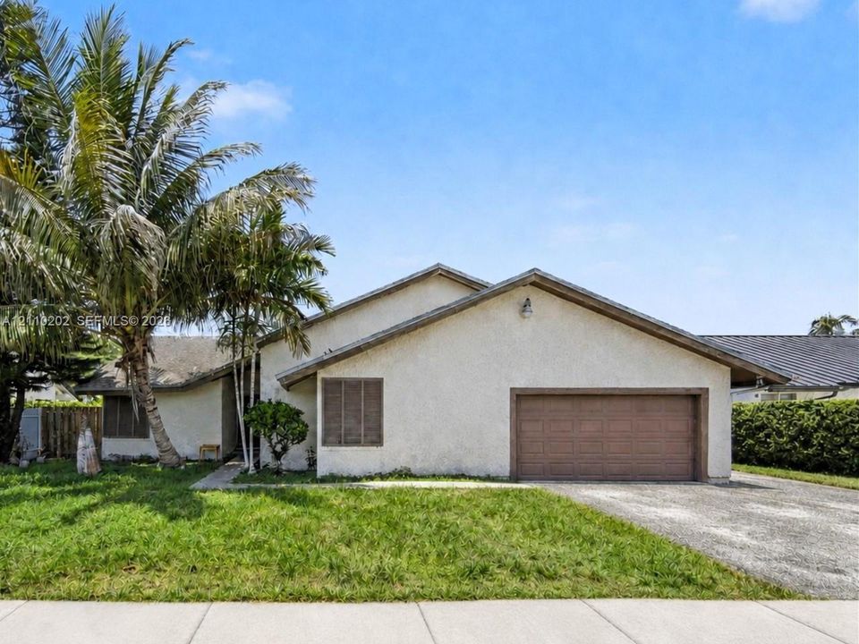 Single-story stucco exterior with a gabled roofline, attached multi-car garage, mature palm trees, and front yard landscaping