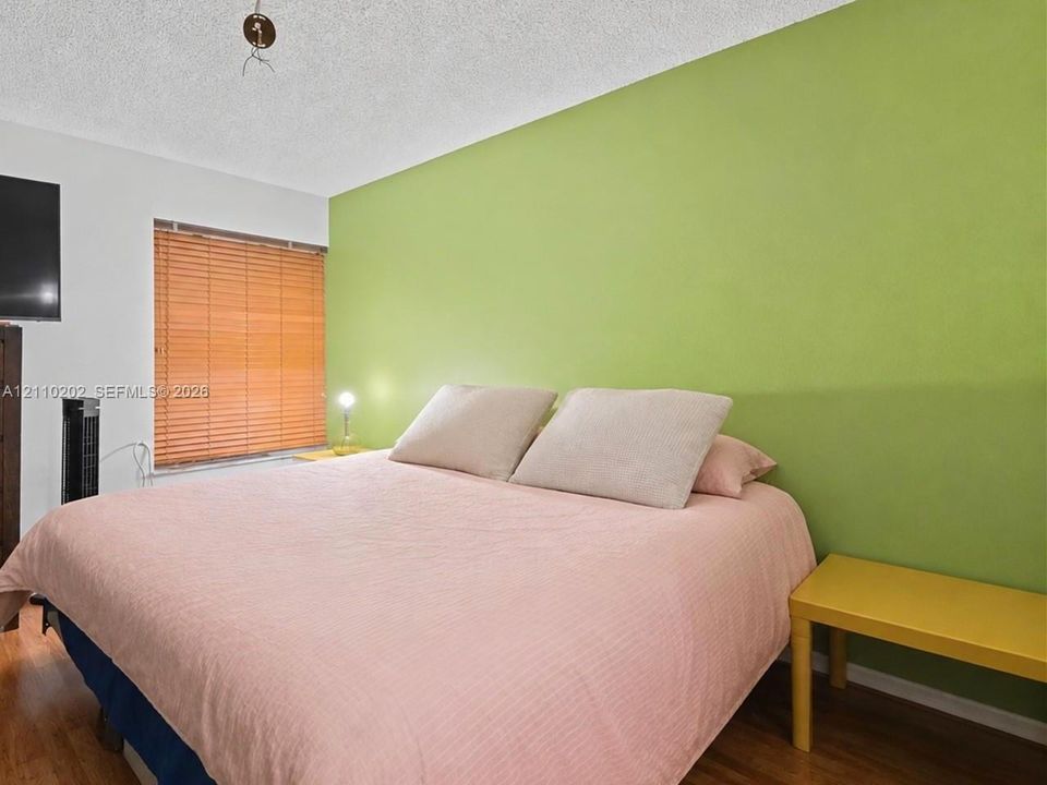 Room featuring wood-finish flooring, a textured ceiling, and a window fitted with horizontal blinds