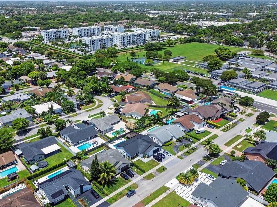 Aerial perspective of suburban residential neighborhood featuring asphalt-paved streets, single-story detached dwellings with gabled roofing, private swimming pools, and mature landscape vegetation