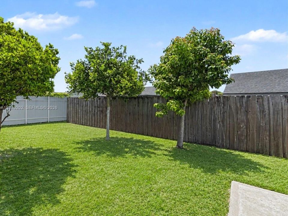 Backyard featuring a manicured lawn, mature trees, and a combination of wood and composite privacy fencing