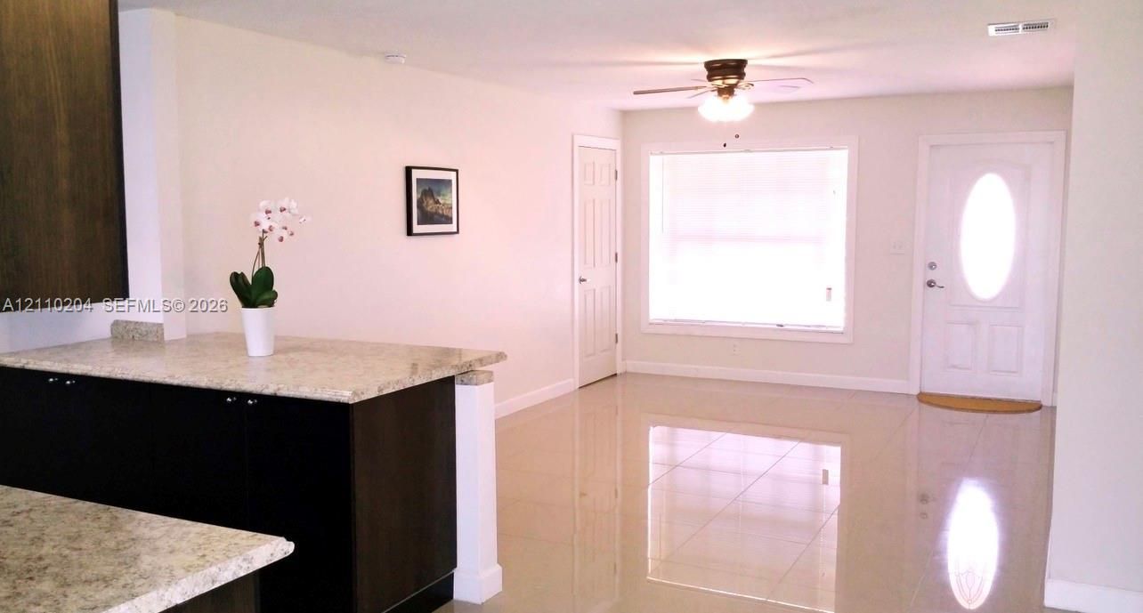 Kitchen featuring dark-finish cabinetry, stone-composite countertops, tile flooring, a ceiling fan with integrated lighting, and a front entry door with a glass inlay