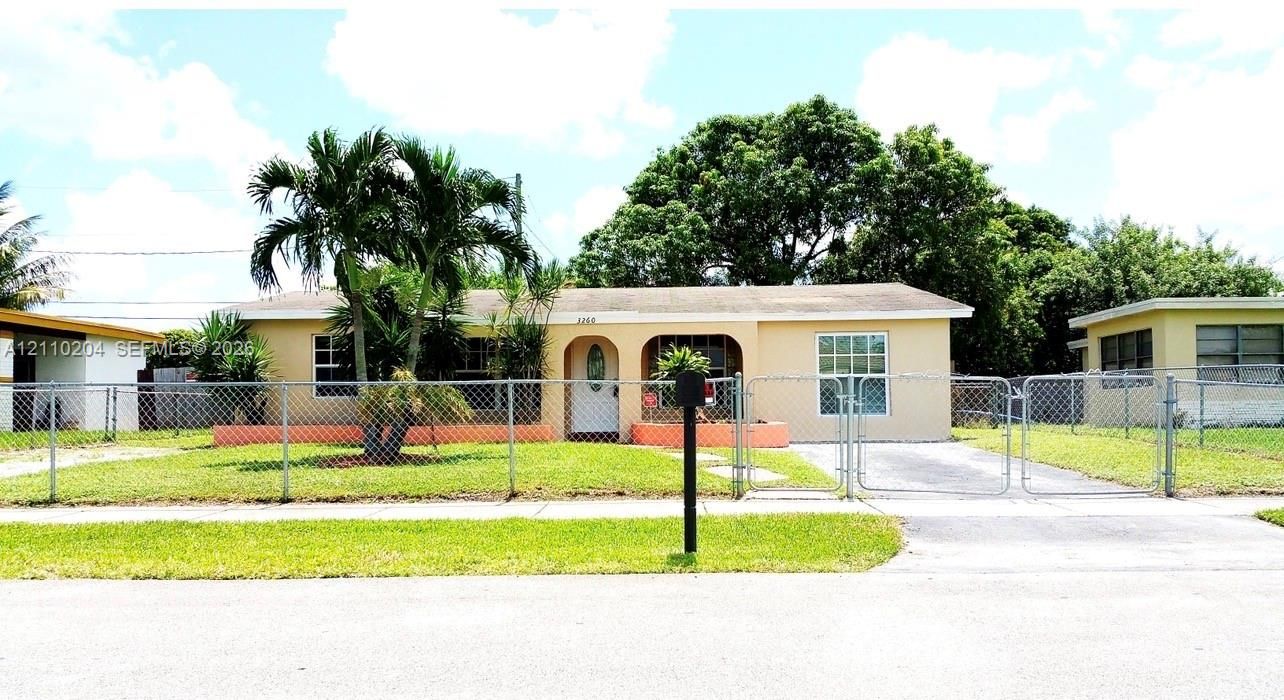 Single-story residence featuring an arched entryway, concrete driveway, and chain-link perimeter fencing