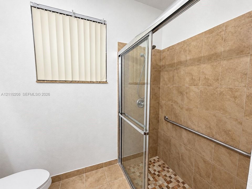 Walk-in shower with sliding glass doors, neutral tile surround, integrated metal grab bar, and a mosaic tile shower floor