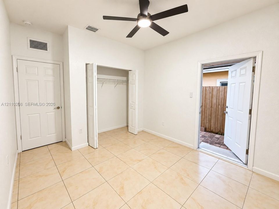 Neutral-toned tile flooring, built-in closet with folding doors, multi-panel entry door, and a ceiling-mounted light fixture with a fan