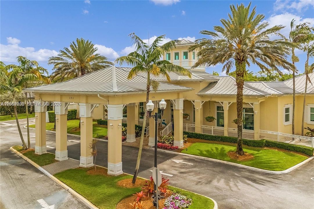 Covered porte-cochère with architectural columns, metal roof, cupola, and landscaped grounds featuring mature palm trees