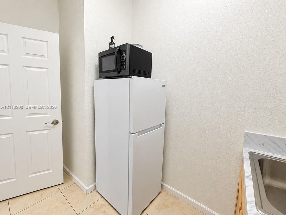 Utility area featuring light-toned tile flooring, a solid-core six-panel door, and a built-in countertop with an integrated stainless steel sink basin