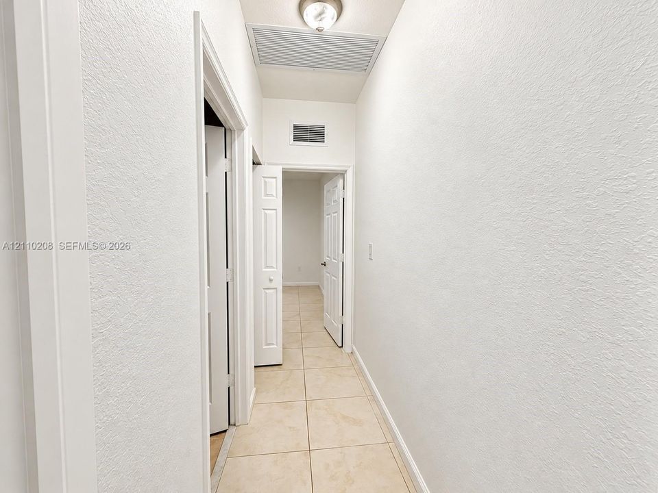 Interior hallway featuring neutral ceramic tile flooring, textured wall finishes, and multi-panel interior doors