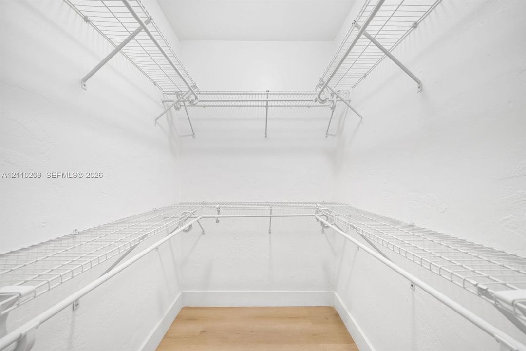 Walk-in closet featuring multi-level white wire shelving and wood-finish flooring
