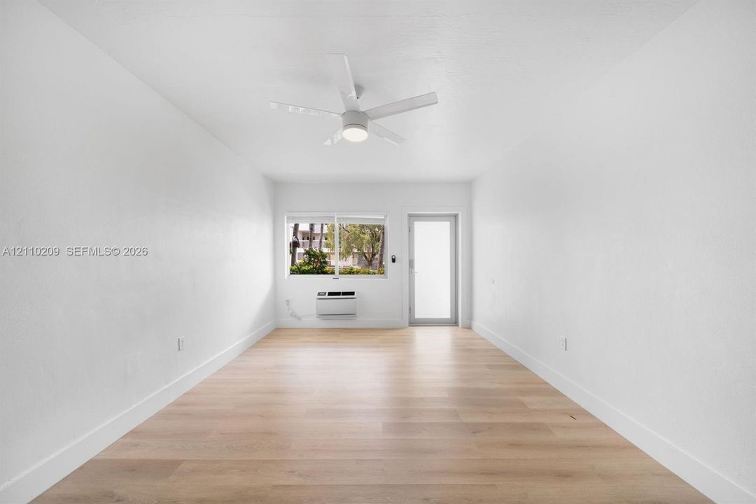 Bright interior featuring wood-finish flooring, a contemporary ceiling fan, a large window, and an integrated wall-mounted climate control unit
