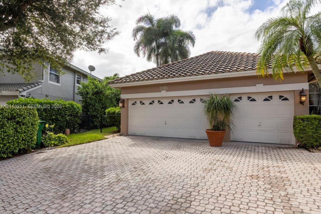Paver driveway leading to a two-car garage with arched decorative windows, tile roof, and exterior wall-mounted carriage lights