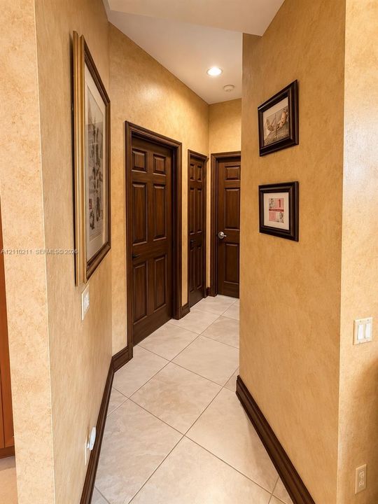 Hallway featuring large-format ceramic tile flooring, solid wood six-panel doors, and recessed lighting