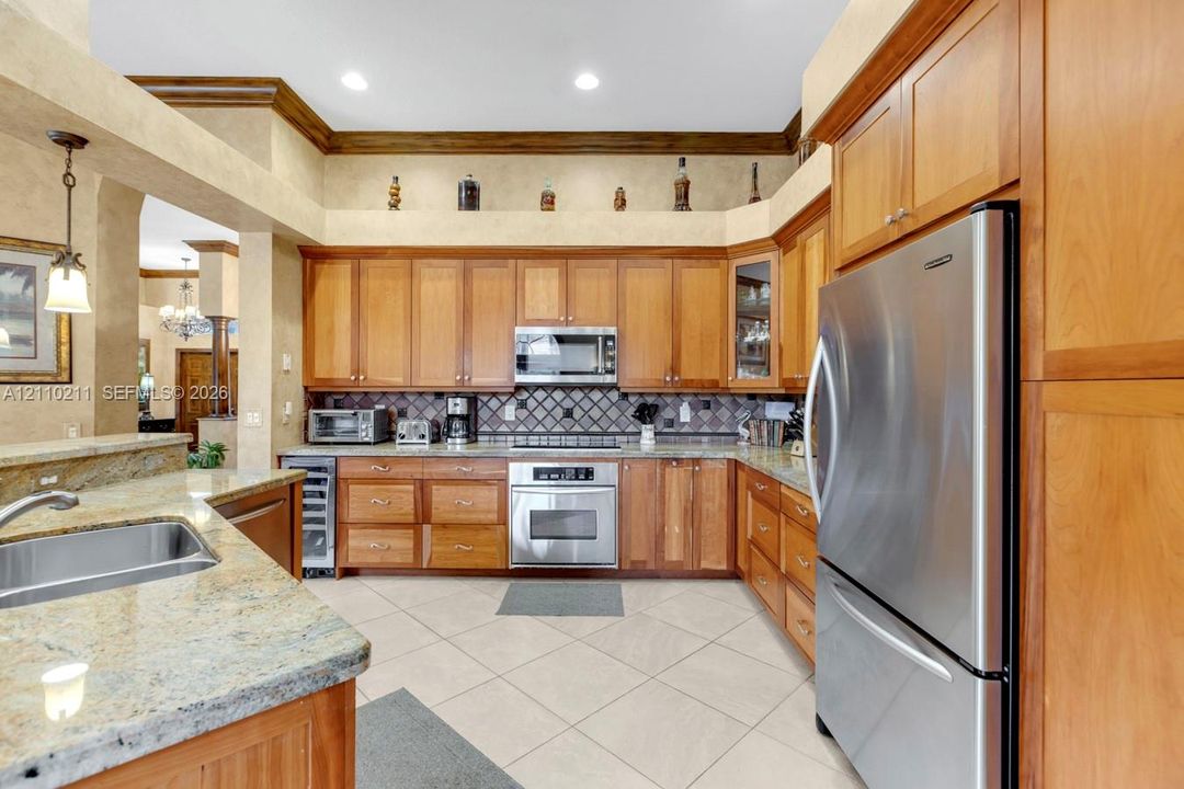 Kitchen featuring stained wood cabinetry, stone countertops, stainless steel appliances, a diamond-pattern tile backsplash, and ceramic tile flooring